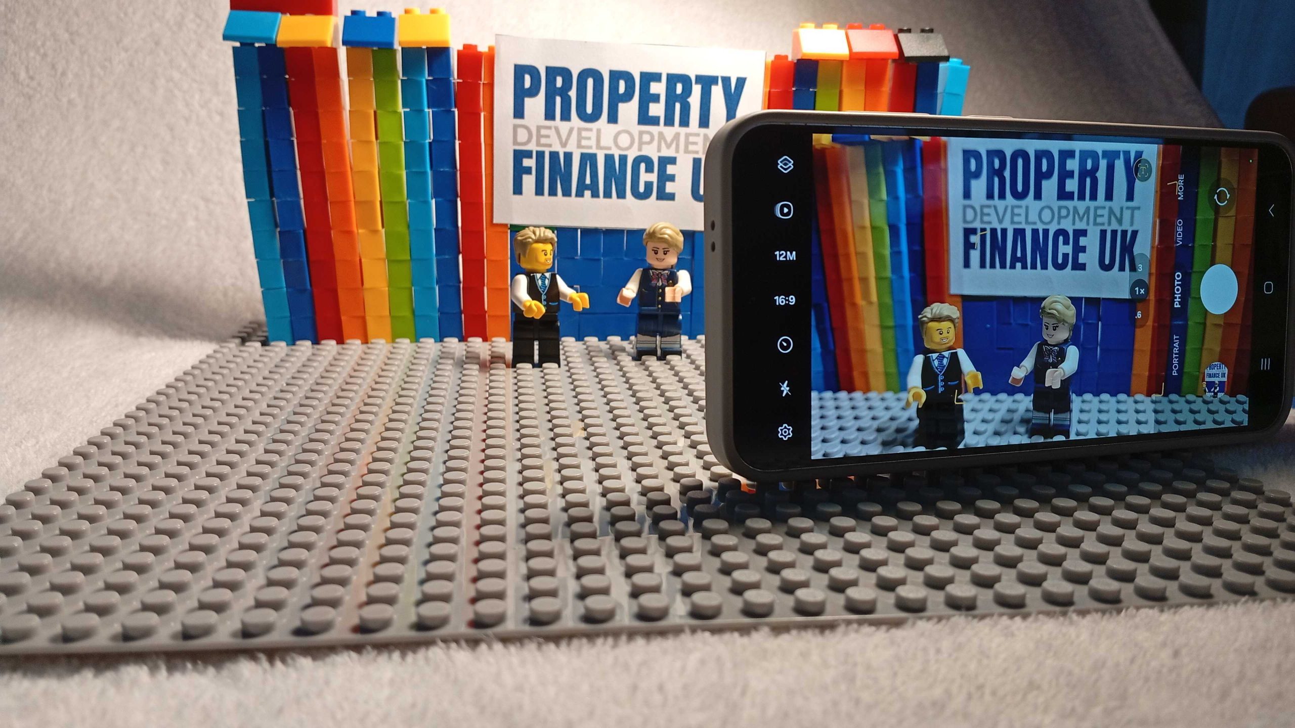 Behind-the-scenes Lego setup with camera filming two developer characters in front of Property Development Finance UK branding